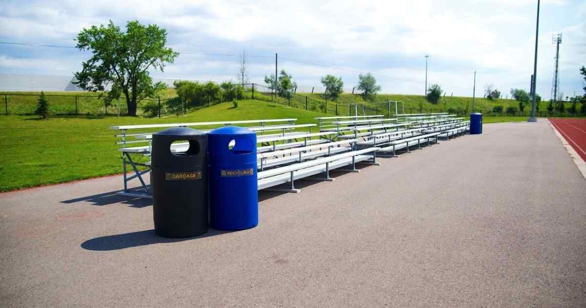 Outdoor bleachers next to garbage and recycling bins on a track and field site.